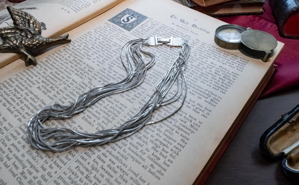 Vintage liquid sterling silver multi-strand necklace bundled together creating a heavy, fluid waterfall effect, resting on an open book.