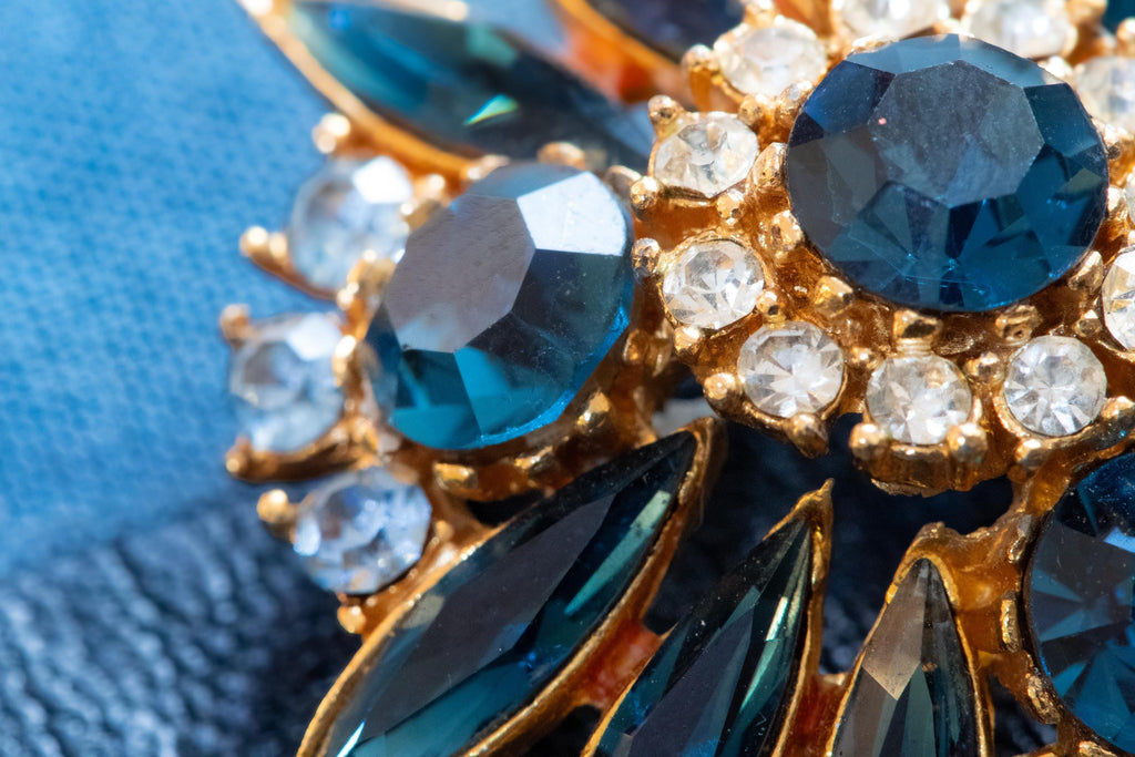 Vintage gold-tone brooch shaped like a flower with multi-layered faceted blue crystals and rhinestones, resting on a blue book.