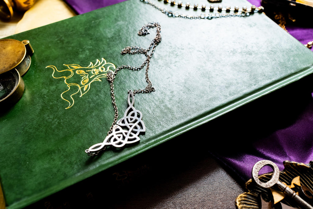 Vintage sterling silver necklace featuring a wide, intricate Celtic knot centerpiece, fully hallmarked from Edinburgh, resting on a green book.