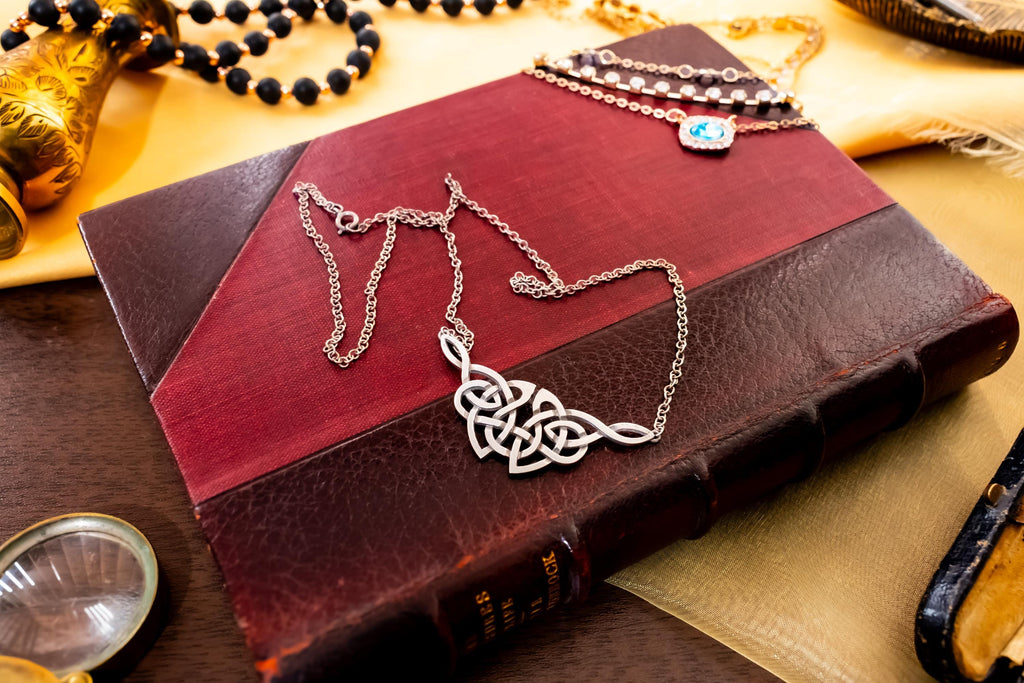 Vintage sterling silver necklace featuring a wide, intricate Celtic knot centerpiece, fully hallmarked from Edinburgh, resting on a green book.