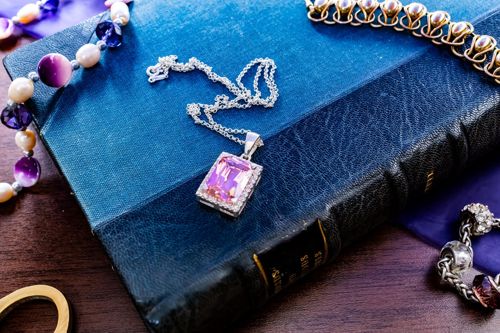 Vintage sterling silver necklace showcasing a large, vibrant emerald-cut pink topaz gemstone surrounded by smaller accent stones, on a green book.