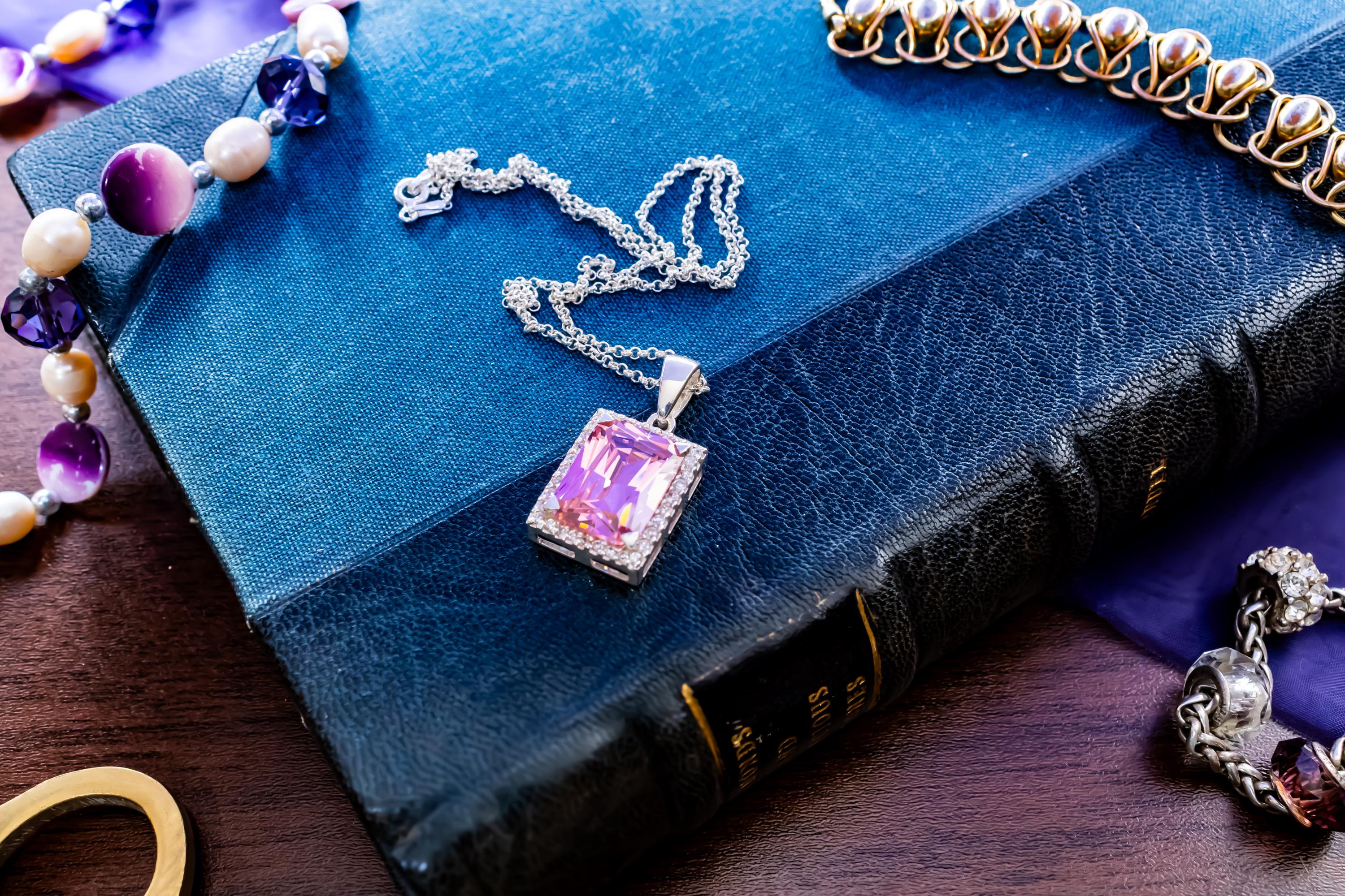 Vintage sterling silver necklace showcasing a large, vibrant emerald-cut pink topaz gemstone surrounded by smaller accent stones, on a green book.
