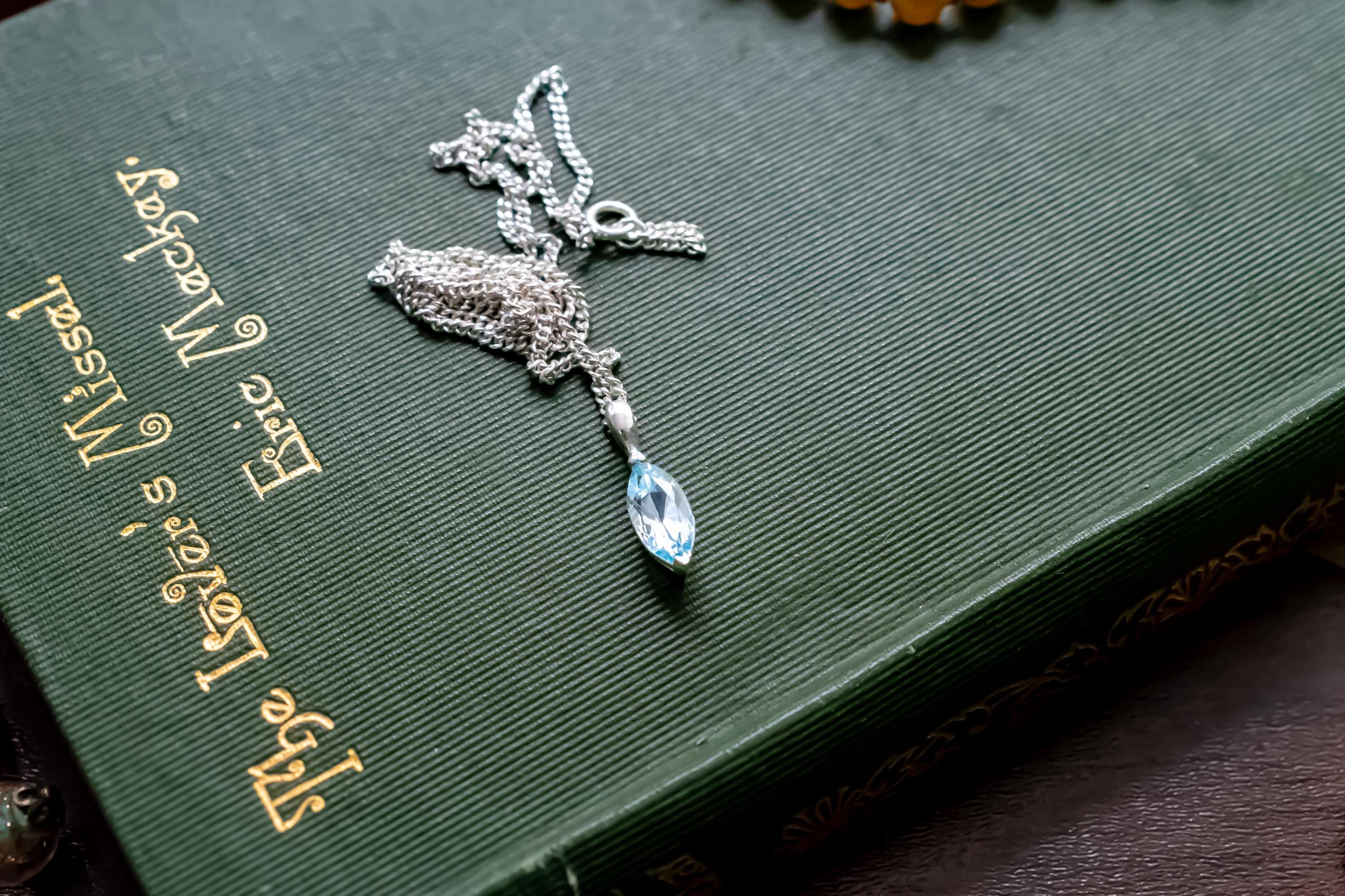 Delicate vintage 925 sterling silver necklace featuring a faceted teardrop-shaped light blue topaz gemstone, draped over a green antique book.