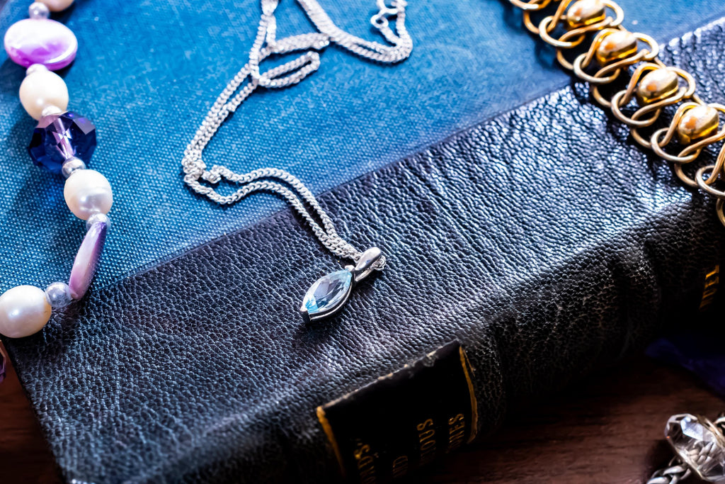 Delicate vintage 925 sterling silver necklace featuring a faceted teardrop-shaped light blue topaz gemstone, draped over a green antique book.