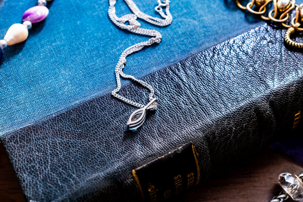 Delicate vintage 925 sterling silver necklace featuring a faceted teardrop-shaped light blue topaz gemstone, draped over a green antique book.
