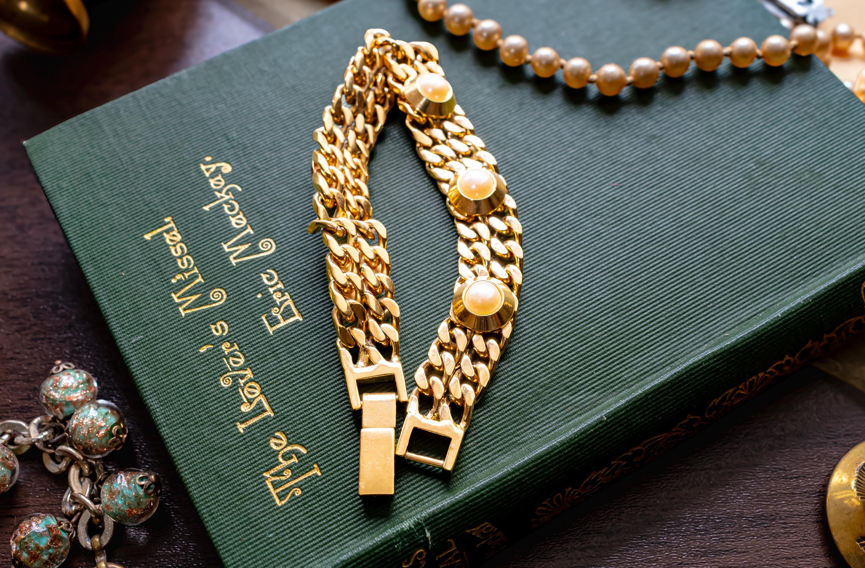 Substantial vintage chunky gold-tone curb link bracelet adorned with large faux pearls in heavy settings, resting on a green vintage book.