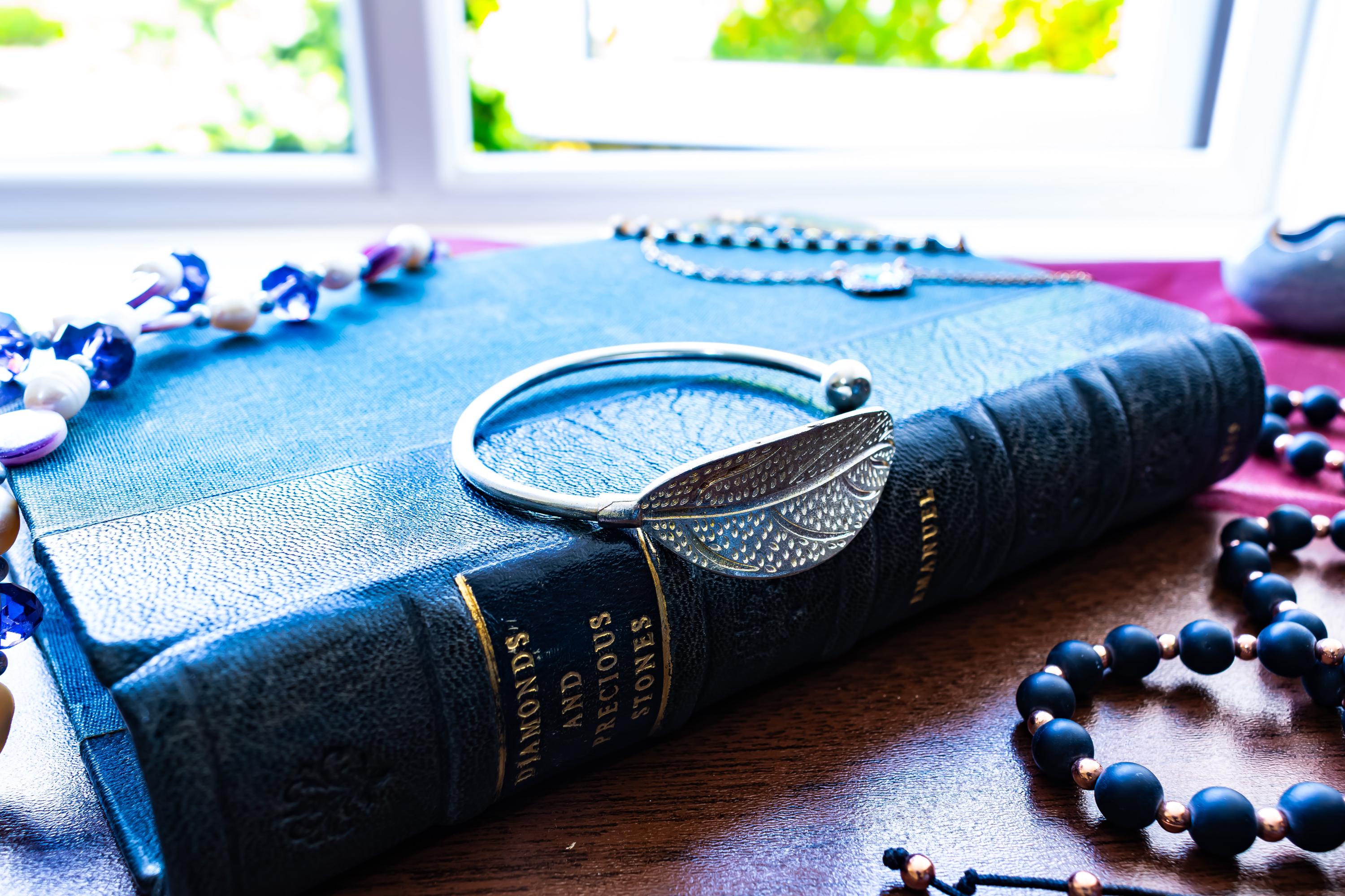 High purity 999 silver torque bangle featuring a detailed, textured feather design, sitting on a blue antique book.