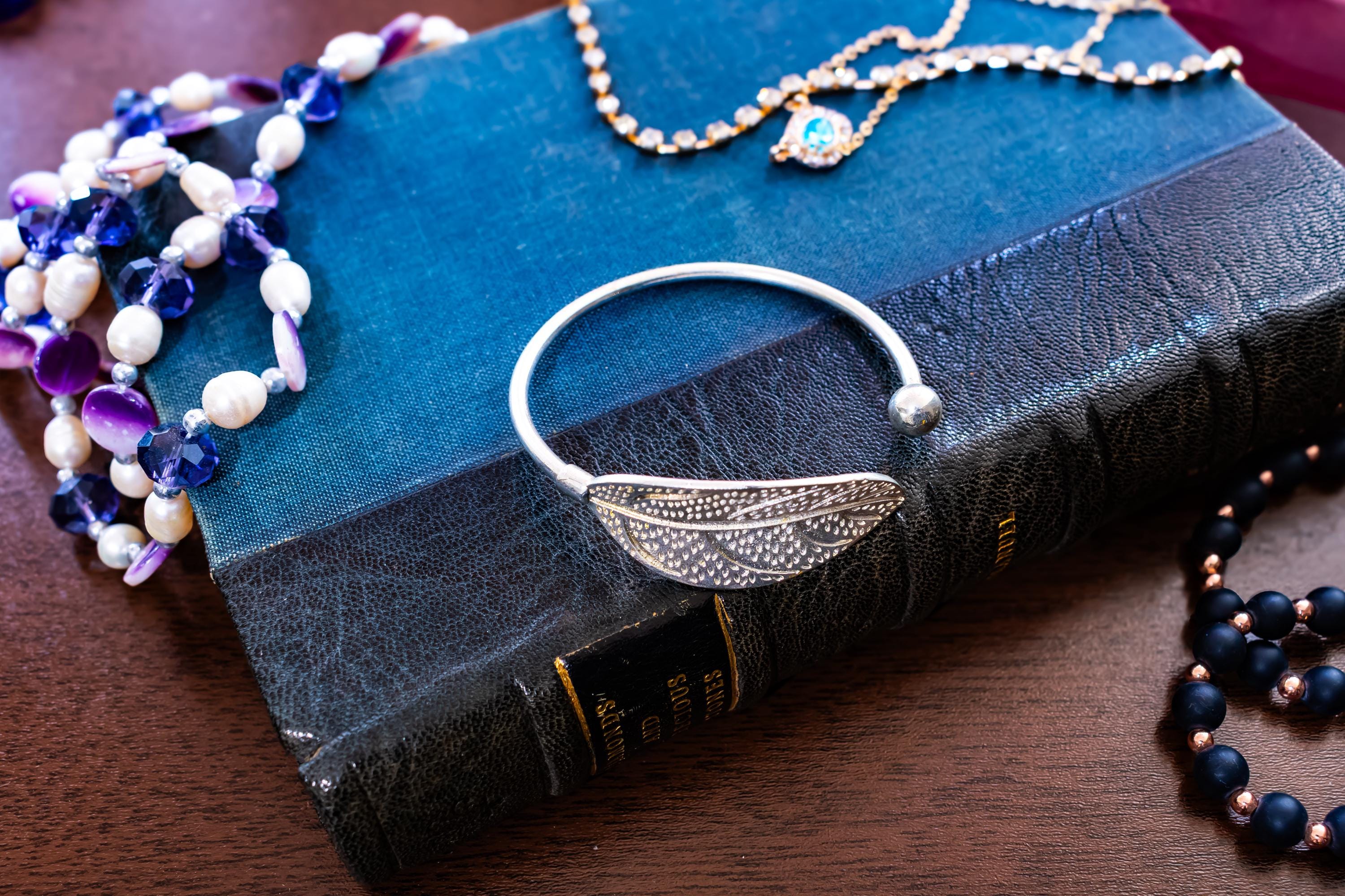 High purity 999 silver torque bangle featuring a detailed, textured feather design, sitting on a blue antique book.