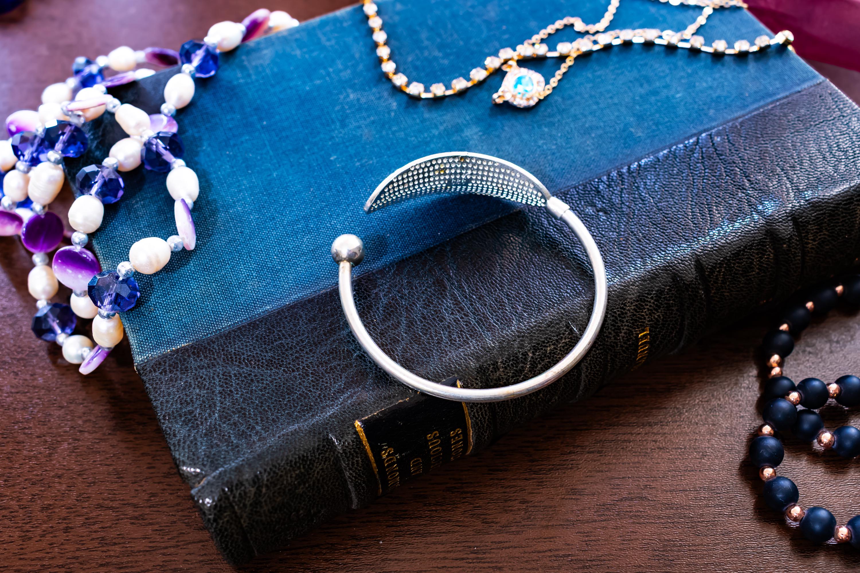 High purity 999 silver torque bangle featuring a detailed, textured feather design, sitting on a blue antique book.