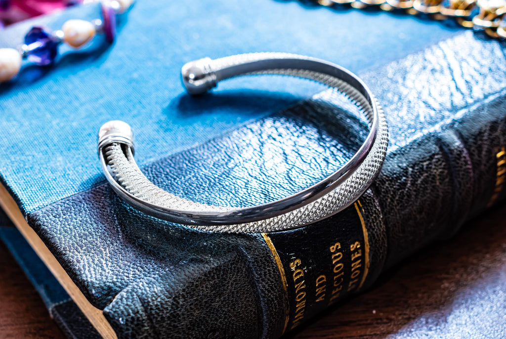 Vintage sterling silver open torque bangle with a woven mesh texture and smooth ball ends, resting on an antique book.