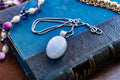 Large oval cabochon luminous moonstone pendant set in 925 sterling silver on a heavy box chain, displayed on a blue vintage book.
