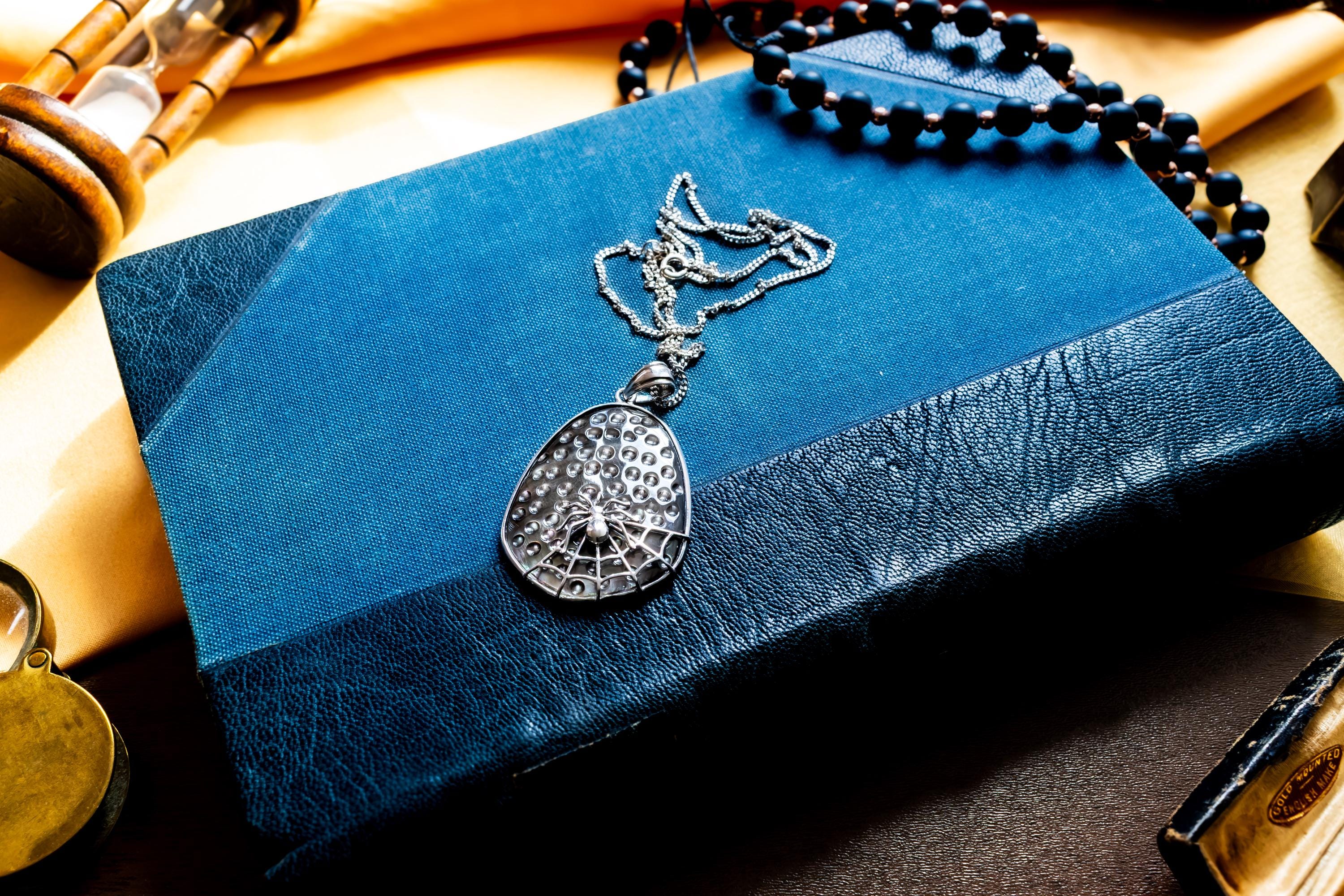 Vintage sterling silver pendant featuring an iridescent black mother of pearl background overlaid with a silver spider and intricate spiderweb design.