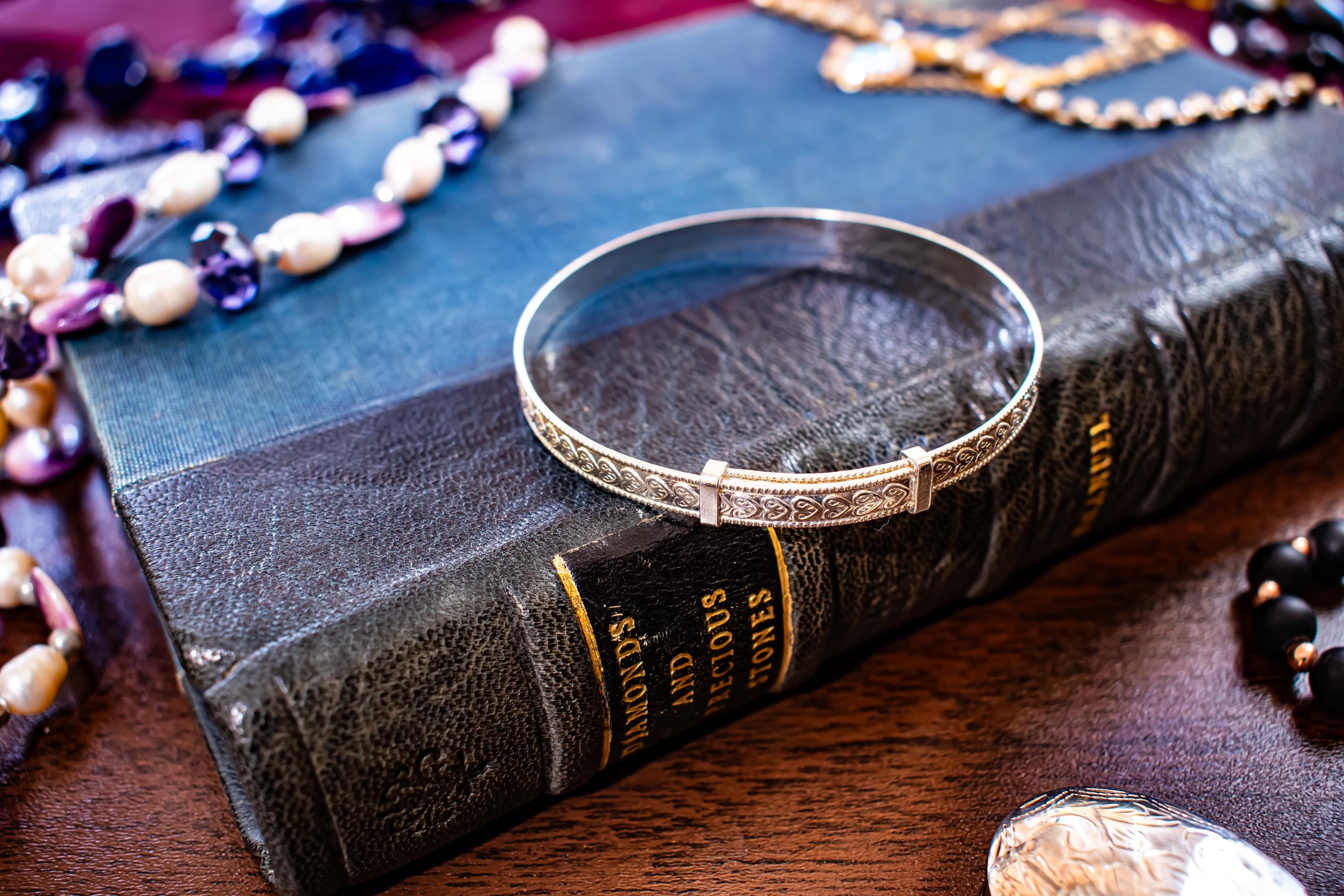 Vintage 1996 sterling silver flexible bangle with intricate engraved patterns along the band, sitting on a vintage blue book.