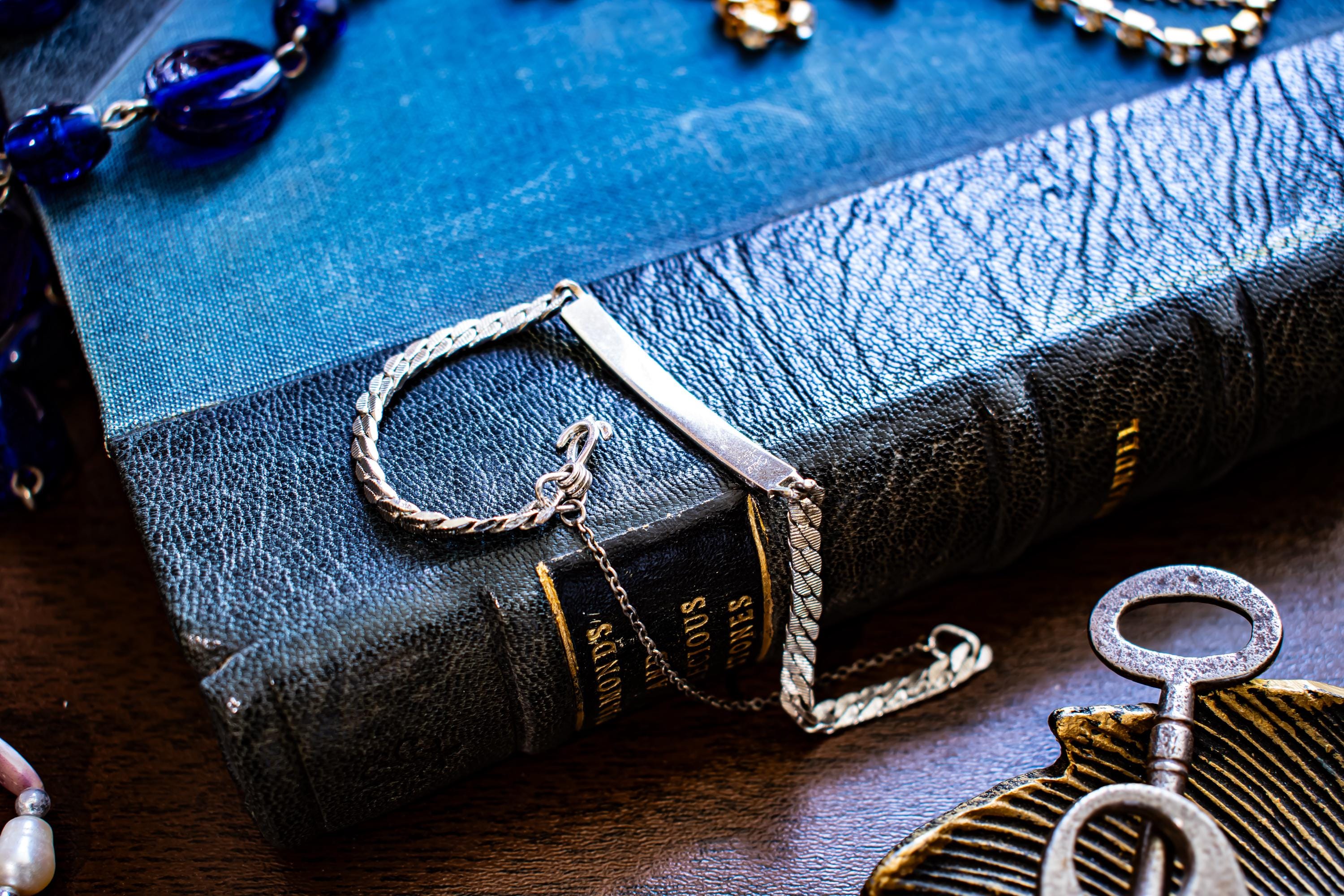 Vintage silver-tone Speidel USA ID bracelet featuring a blank rectangular plate, interlocking sister hook clasp, and safety chain, resting on an antique book.